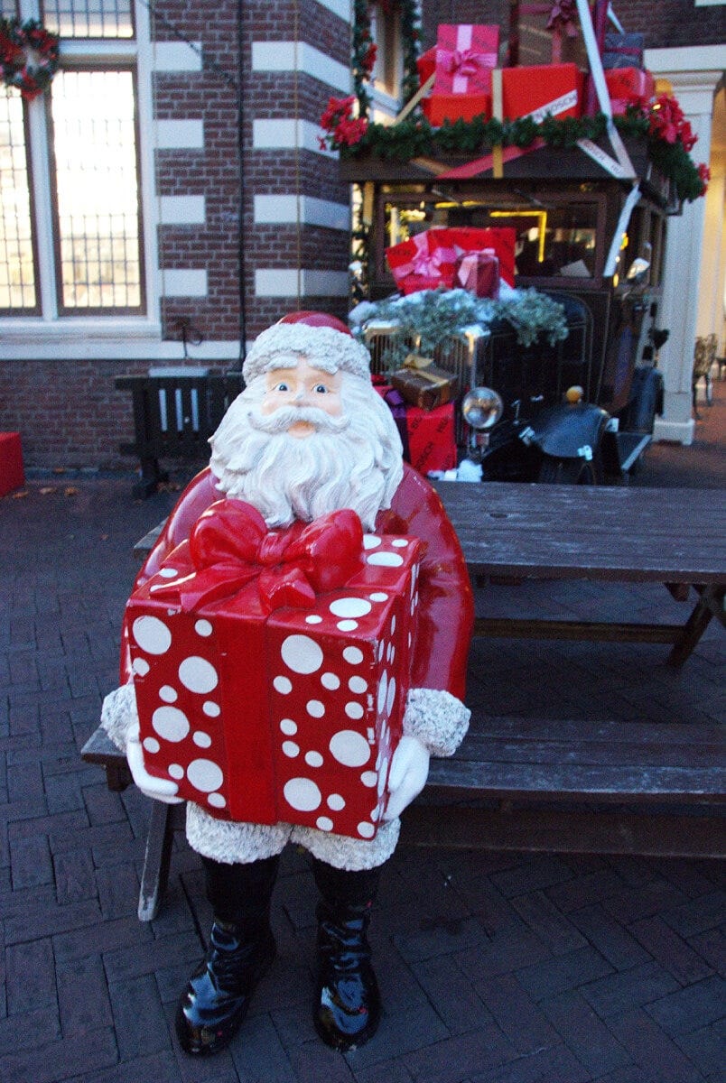 大きなプレゼントを持ってイスに座るサンタクロース。隣に座って一緒にパチリ