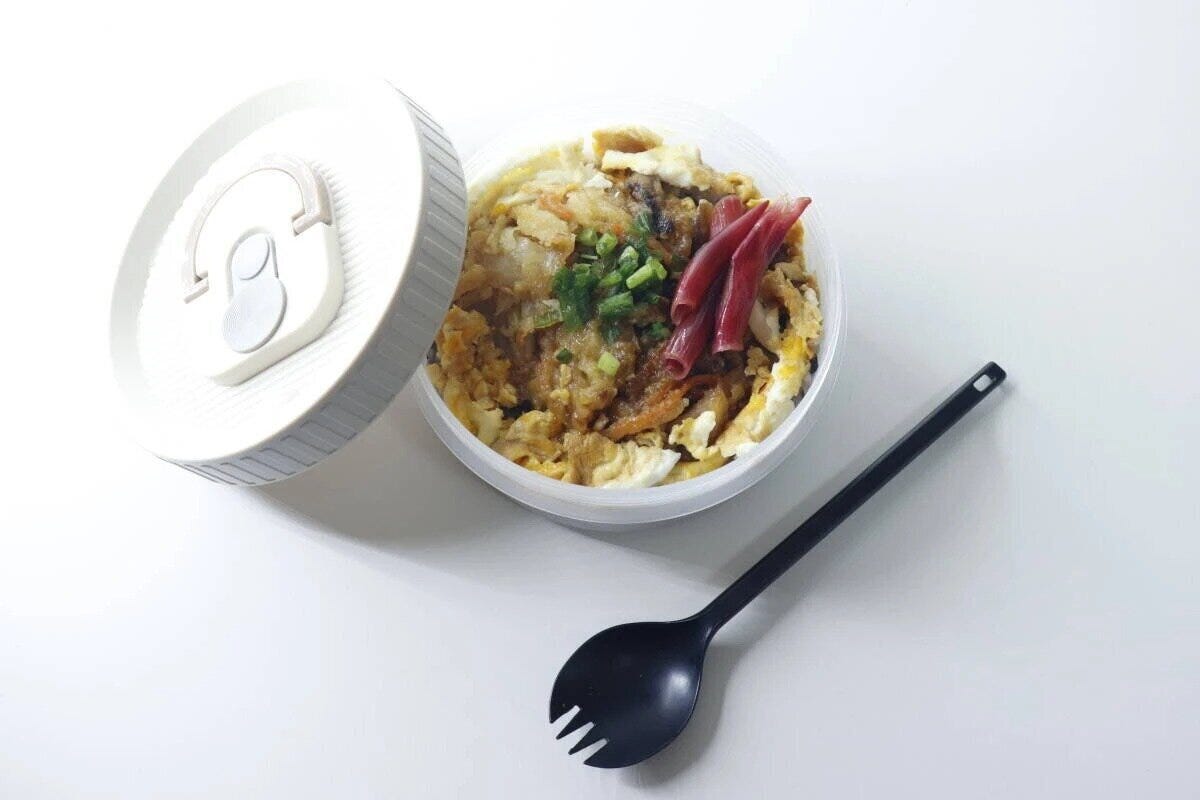 丼ものが盛られた丸い弁当箱とフタ、黒いスプーン
