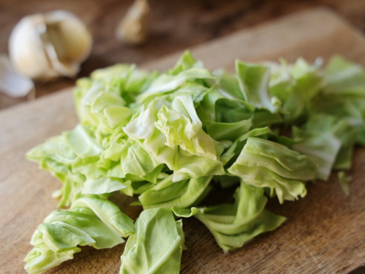まな板の上にざく切りにした春キャベツとにんにくが置かれた下準備の写真