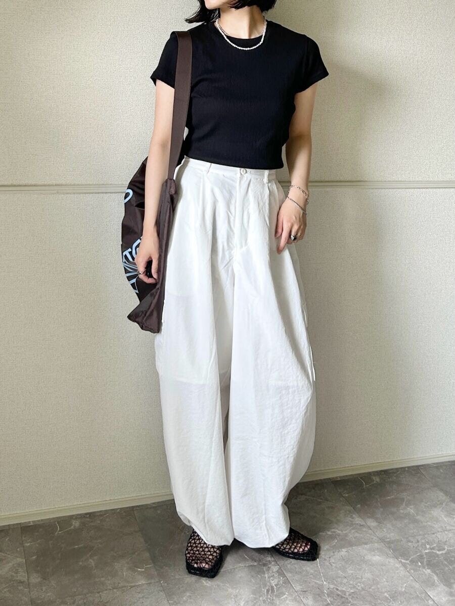 黒いリブミニTシャツと白いカーゴパンツを着用し、茶色のバッグを肩にかけた女性の全身 黒いリブミニTシャツと白いカーゴパンツを着用し、茶色のバッグを肩にかけた女性の全身