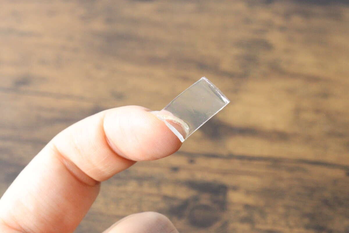 指でつまんだ透明で厚みのある強力両面粘着ゲルテープの切れ端