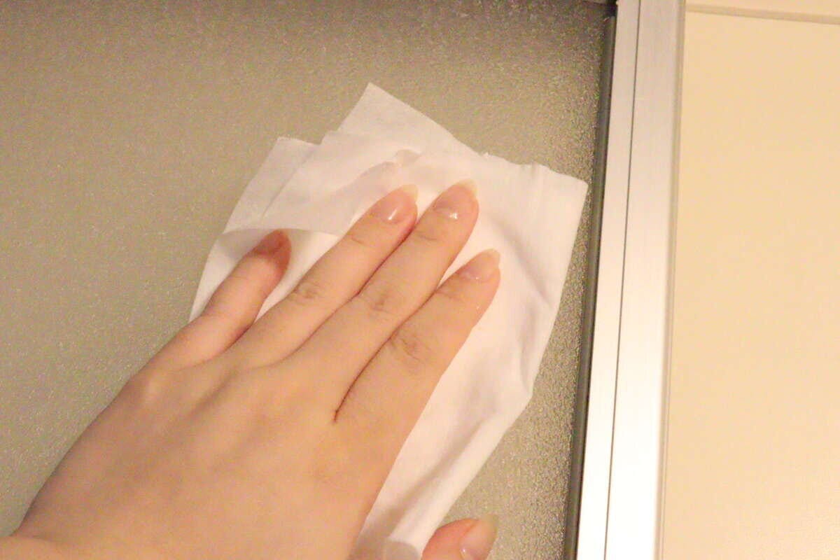 女性の手が浴室の曇りガラスの壁面をシートで拭いている
