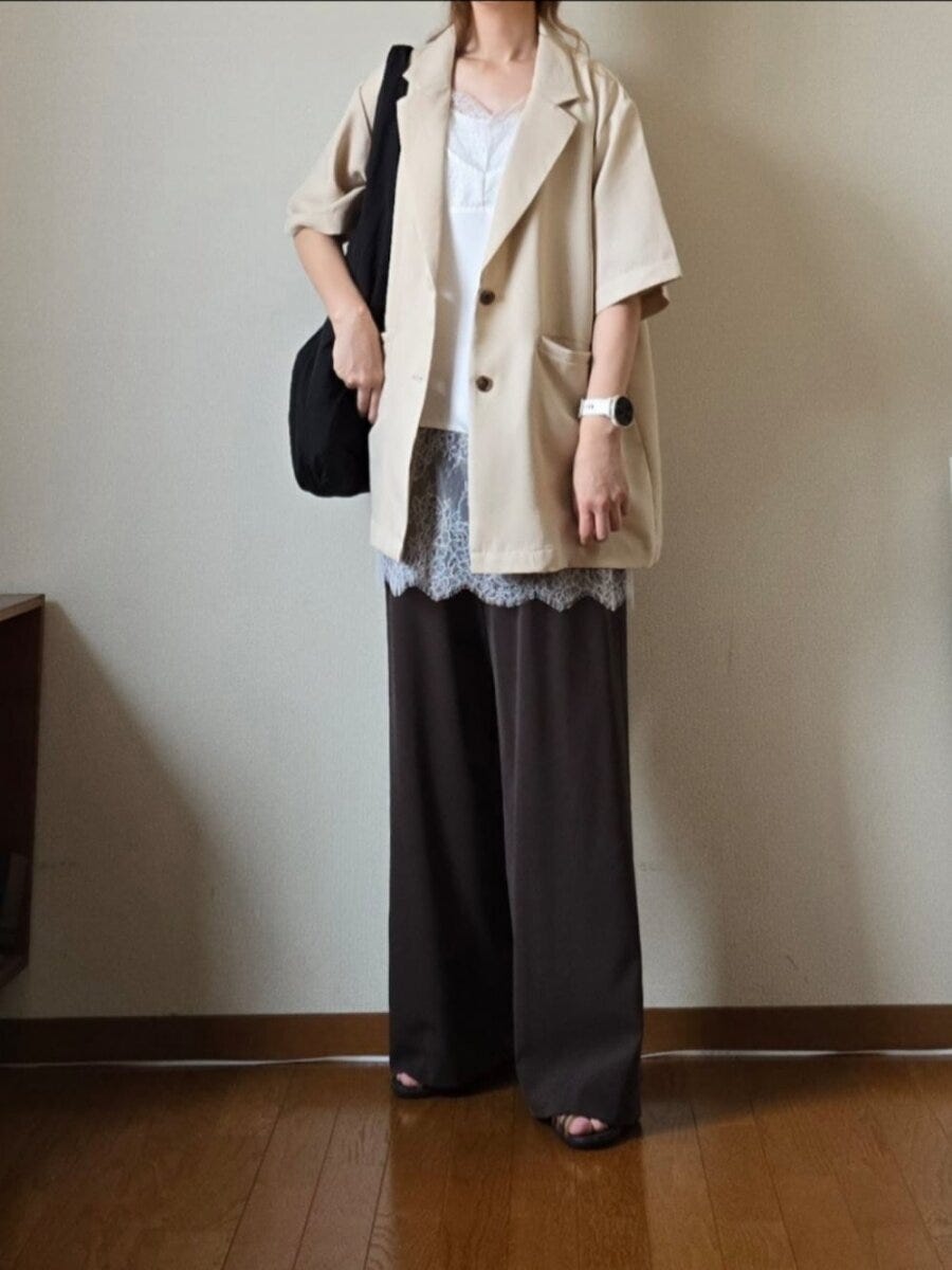 ベージュの半袖ジャケットとモカ色ワイドパンツ、レースキャミソールを着た女性。