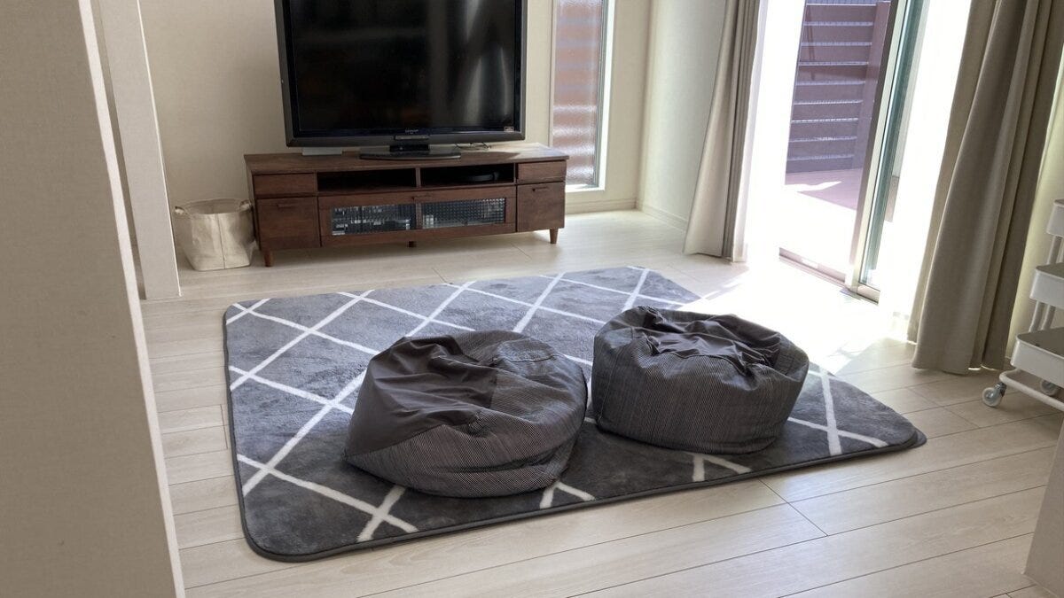 木製テレビ台と薄型テレビの前に幾何学模様のグレーのラグを敷き、グレーのビーズクッションを2つ並べた明るいリビング