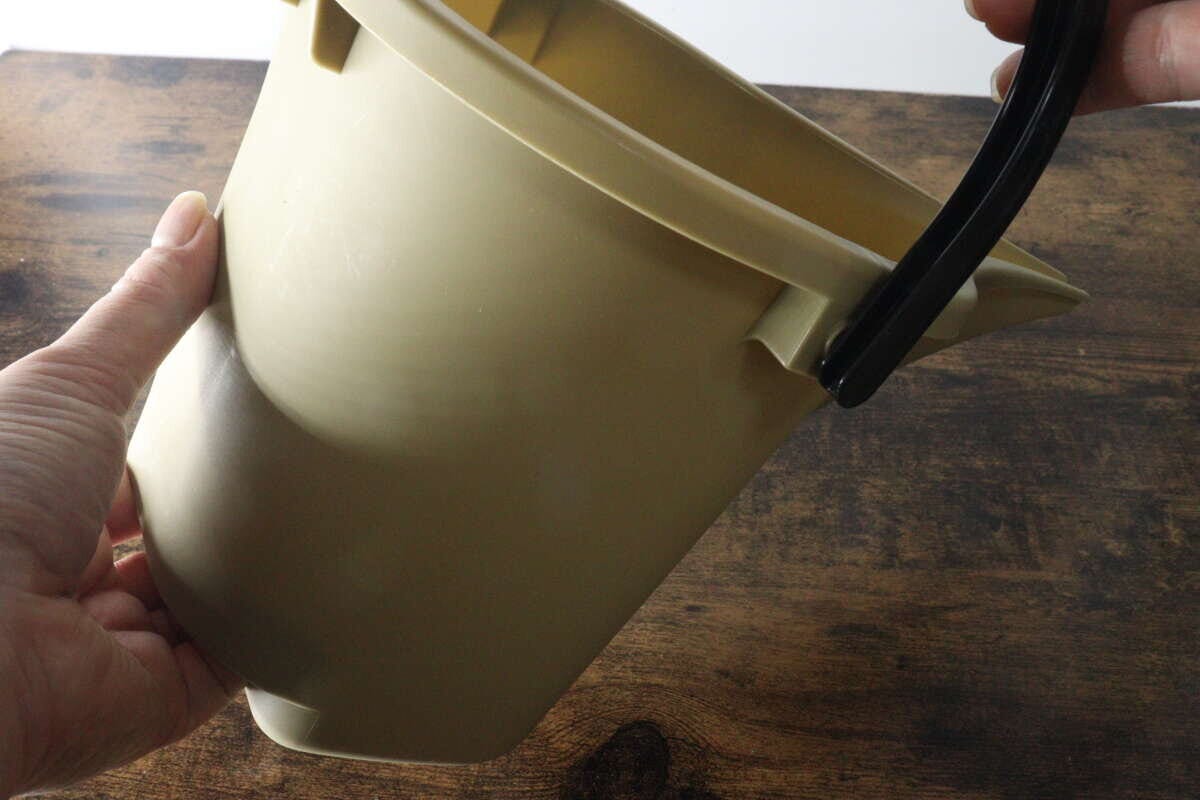 手がダイソー水差しバケツの底のくぼみに指をかけて持ち上げている
