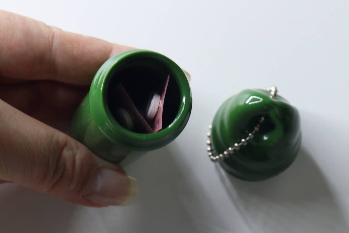 女性の手が緑色の小物入れキーホルダーの本体を持ち、中にシート状の薬が収納されている様子