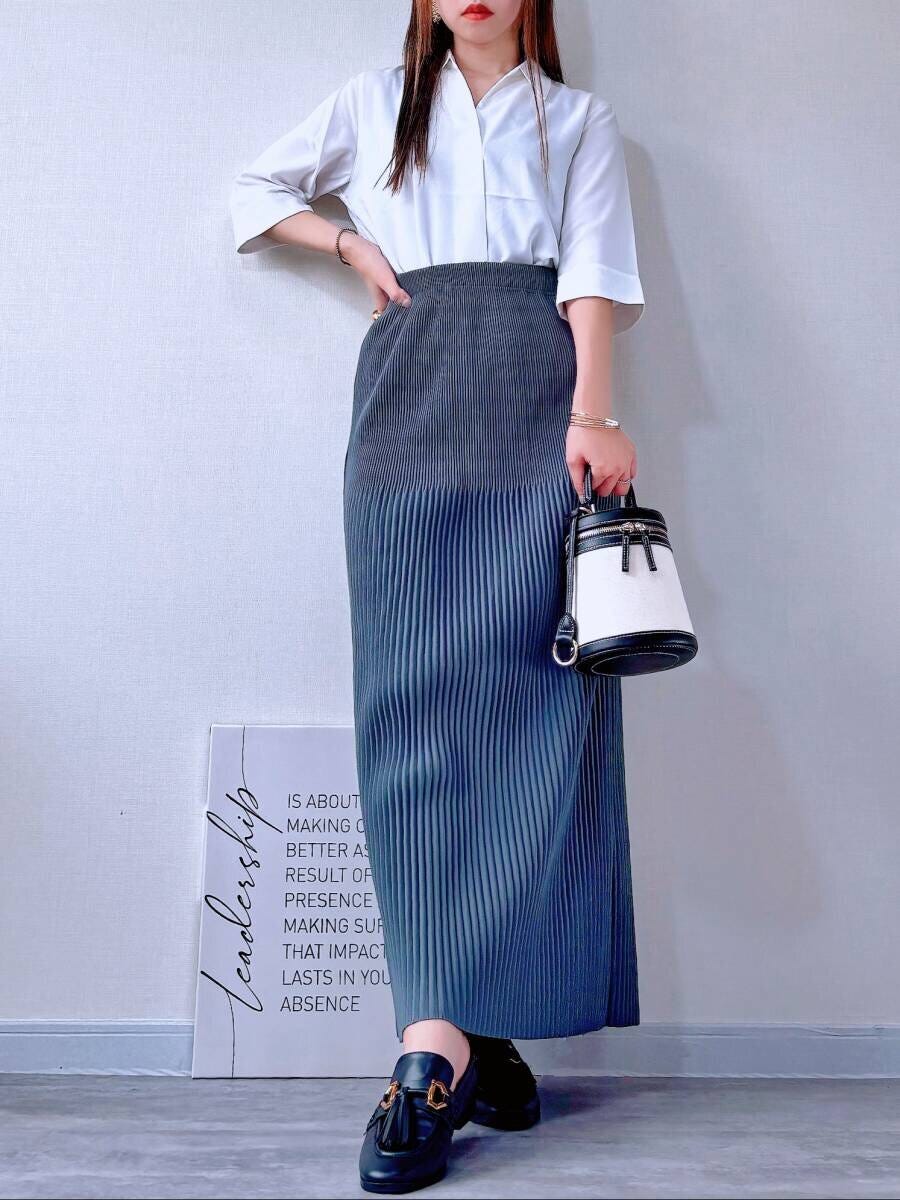 白いブラウスを前だけインし、グレーのプリーツスカートを合わせた女性の全身 白いブラウスを前だけインし、グレーのプリーツスカートを合わせた女性の全身