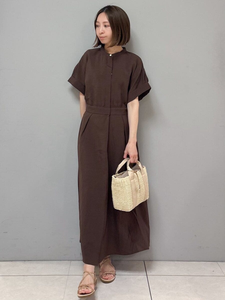 ダークブラウンのシャツワンピースを着た女性が、かごバッグを持ち横を向く