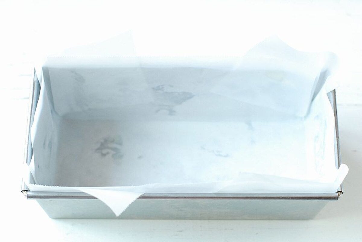 ステンレス製のパウンド型に白いオーブンシートを敷き込んだ下準備の俯瞰写真