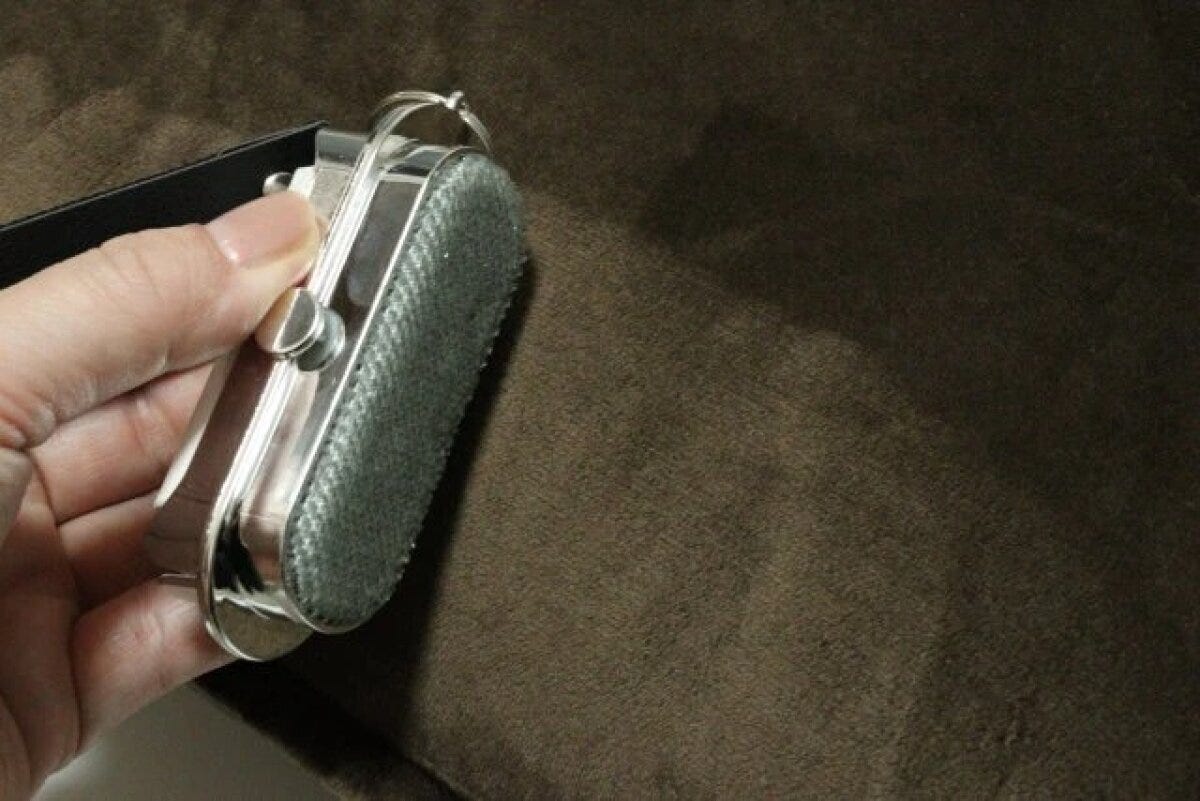 手で持ったほこり取りのブラシ部分で茶色い布をこすっている