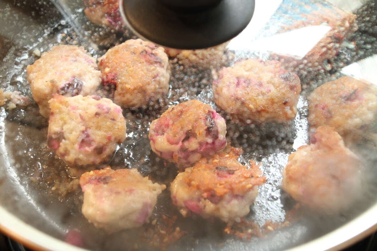 フライパンで焼いている鶏つくねにガラスの蓋をして蒸し焼きにしている調理工程
