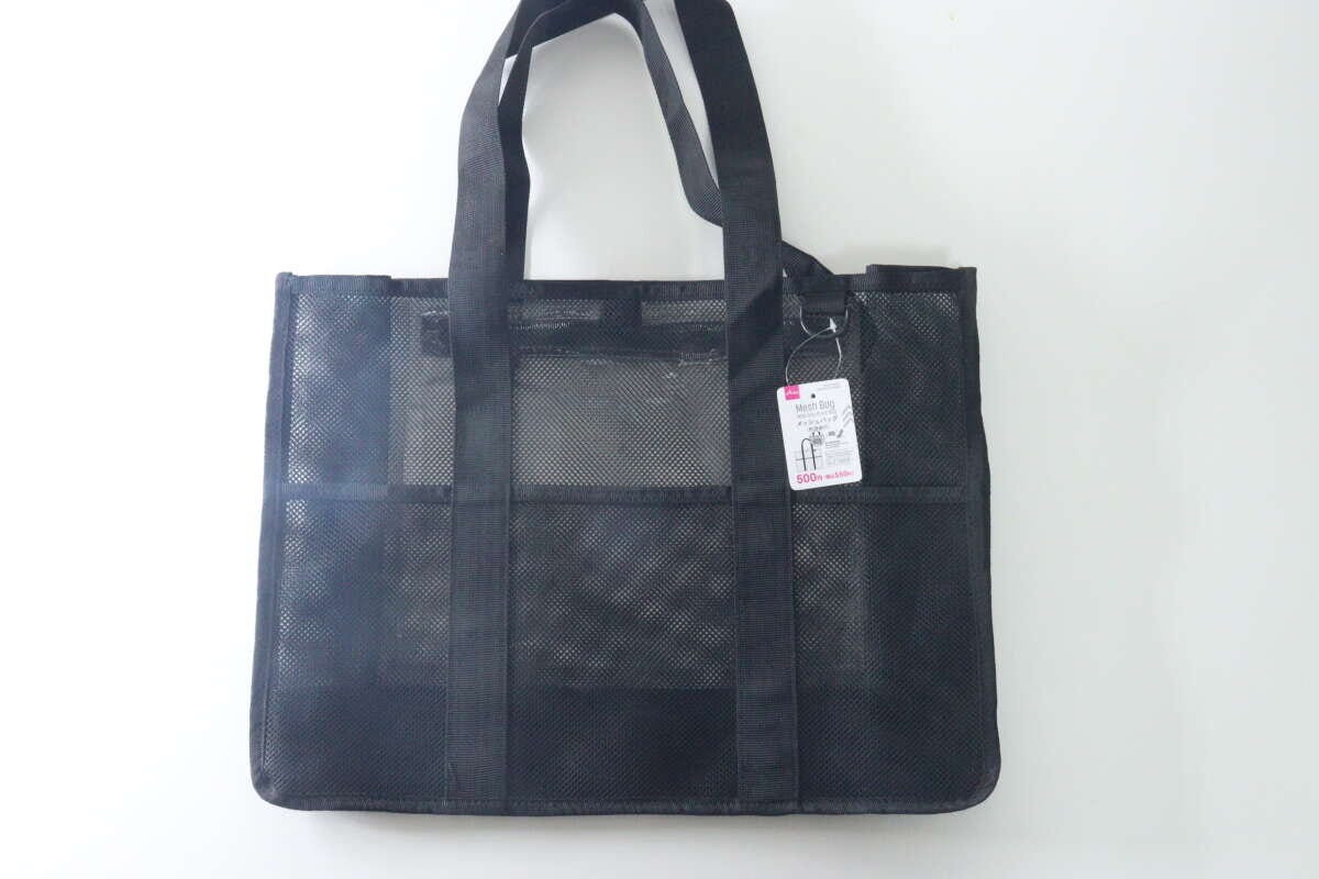 白い背景に置かれた黒いメッシュ素材のトートバッグ。商品タグが付いている。