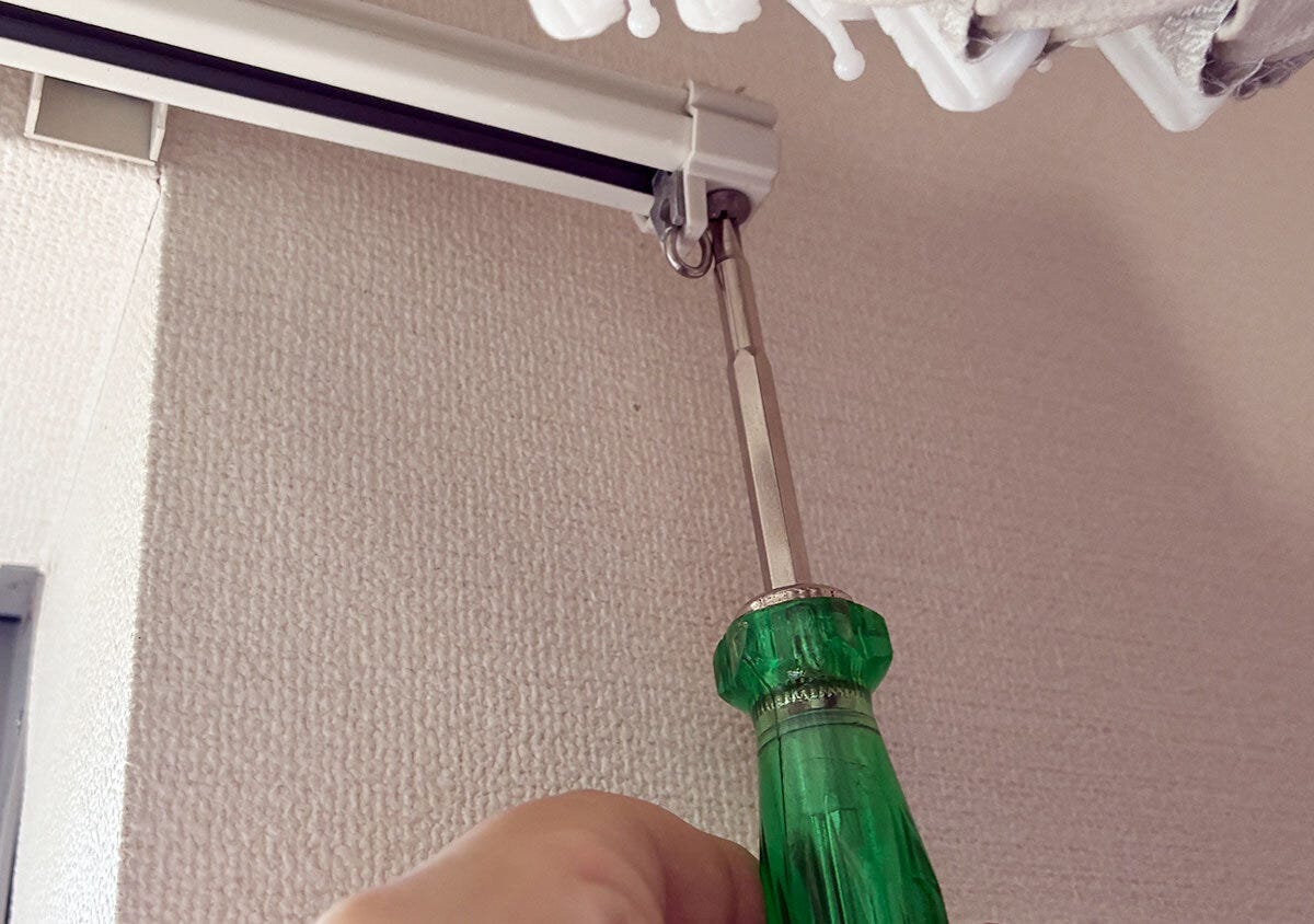 緑色のドライバーを使ってカーテンレールのキャップストップを外している手元