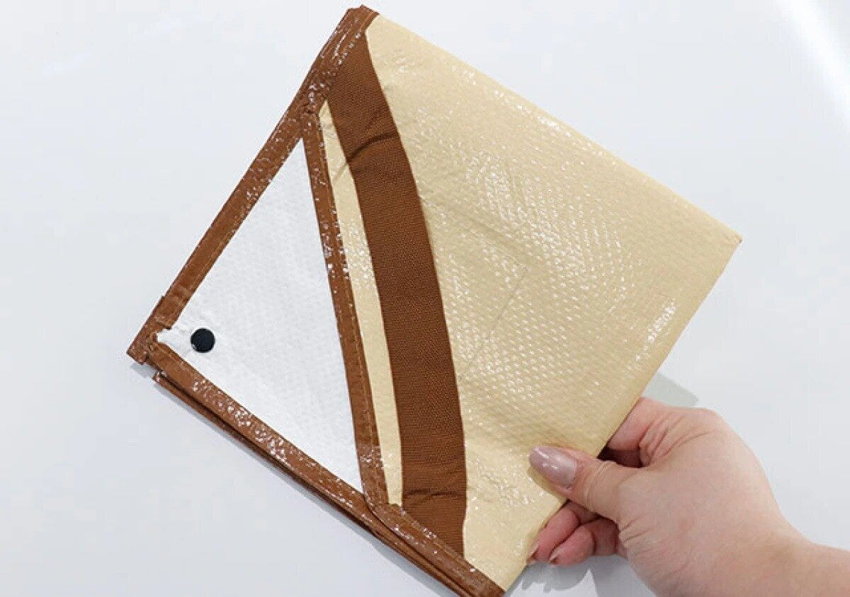 女性の手がベージュと茶色の折りたたまれたシートを持っている 女性の手がベージュと茶色の折りたたまれたシートを持っている