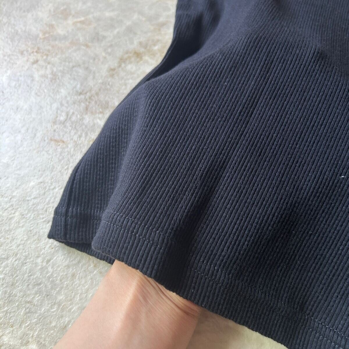 黒いリブミニTシャツの裾部分を指でつまんで生地のアップを見せている 黒いリブミニTシャツの裾部分を指でつまんで生地のアップを見せている