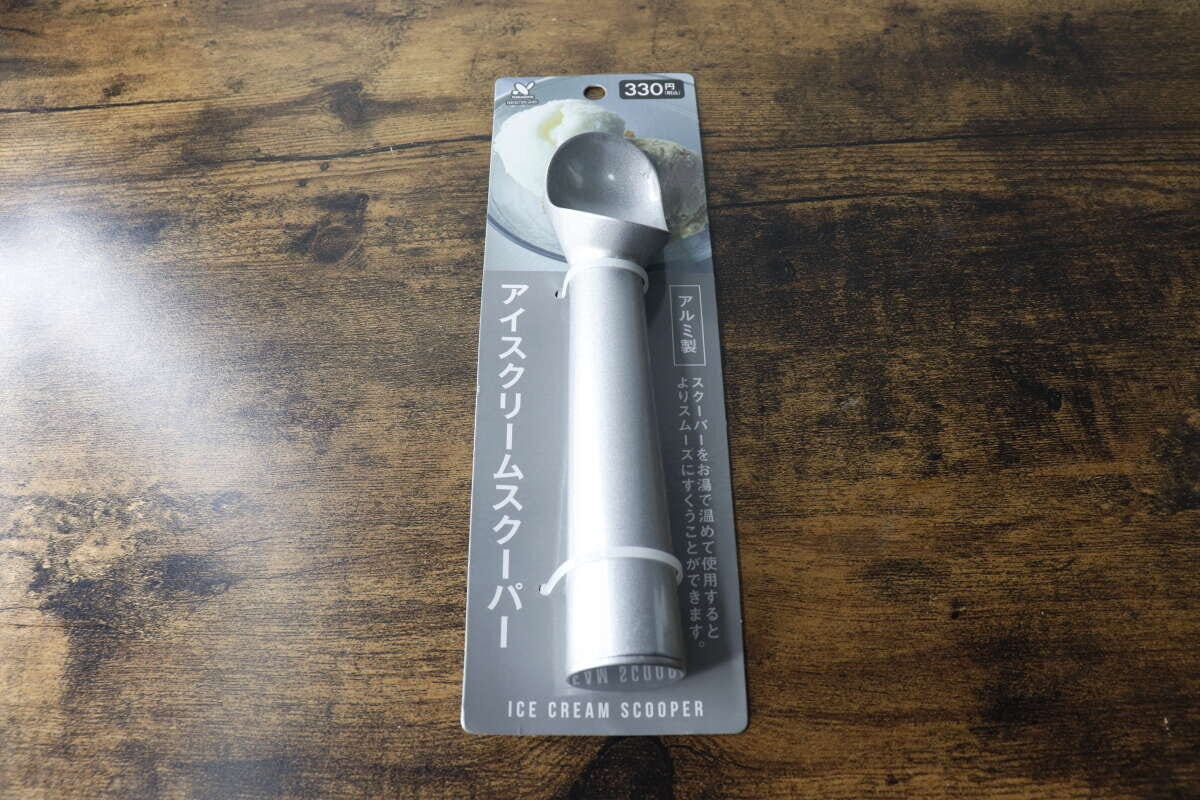 パッケージに入ったアルミ製アイスクリームスクーパーが木目のテーブルに置かれている パッケージに入ったアルミ製アイスクリームスクーパーが木目のテーブルに置かれている