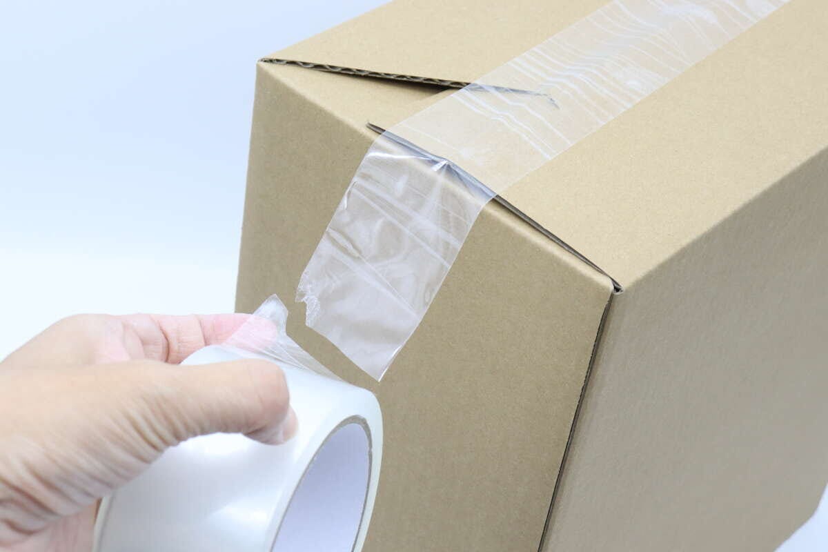 ダンボール箱に透明な梱包テープを貼り、手でちぎっている途中 ダンボール箱に透明な梱包テープを貼り、手でちぎっている途中