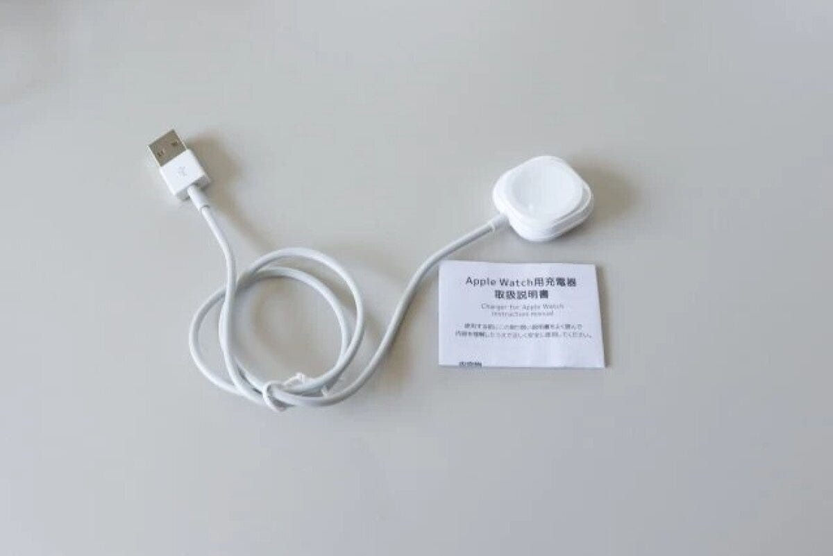 白いスマートウォッチ充電器とUSBケーブル、取扱説明書が写っている