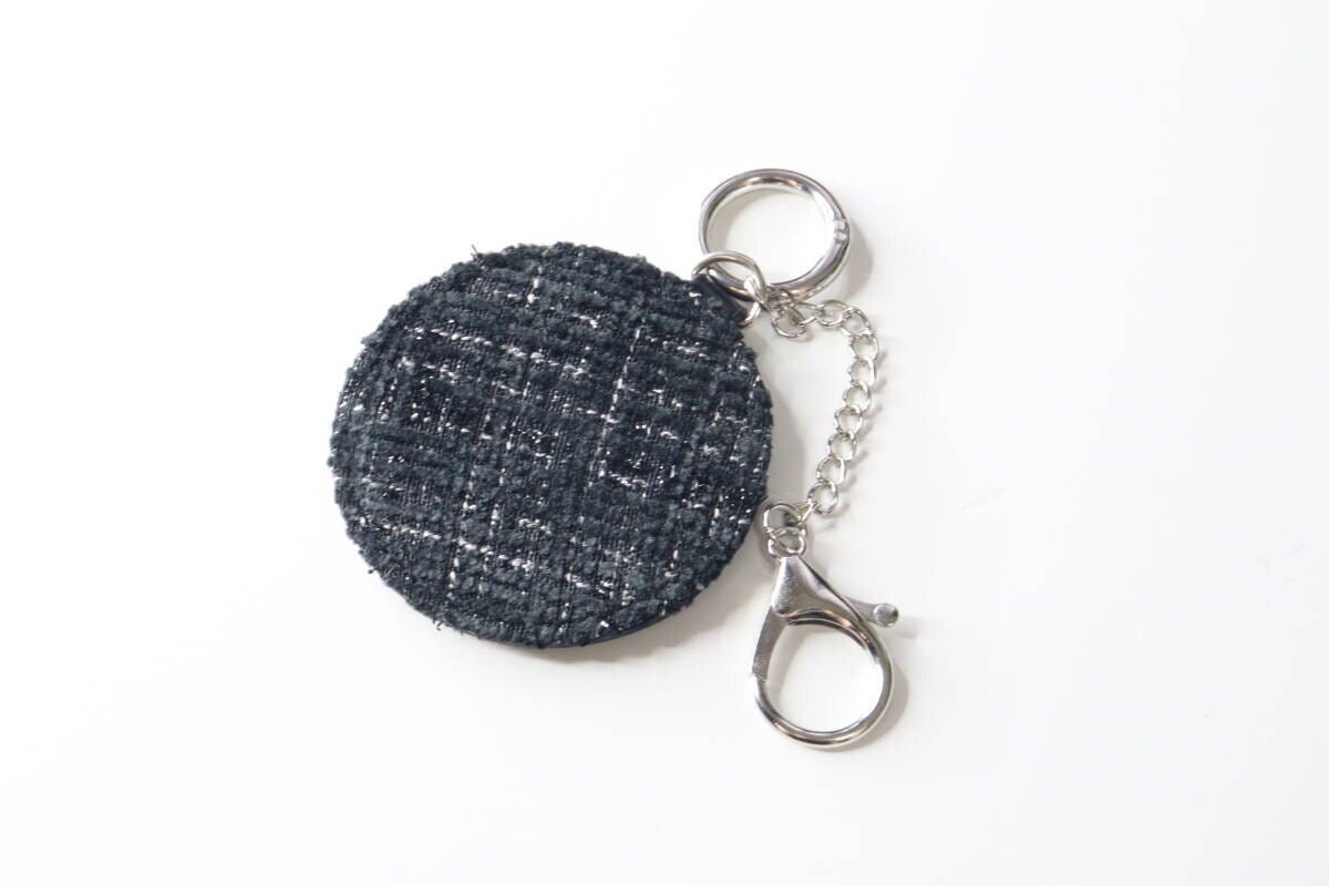 白い背景に置かれたツイード柄の黒い丸型鏡キーホルダーと金具 白い背景に置かれたツイード柄の黒い丸型鏡キーホルダーと金具