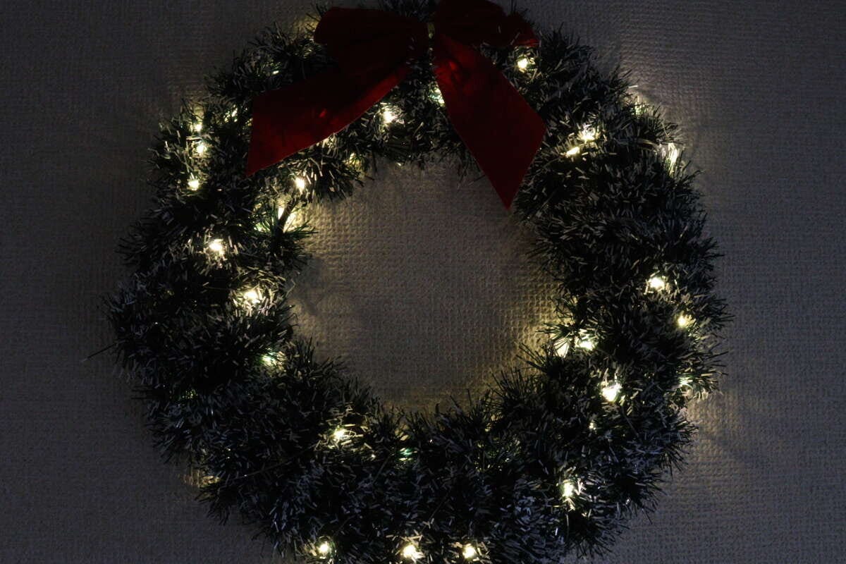 クリスマスリースにストリングライトを巻き付け、暗い部屋で点灯させた様子。 クリスマスリースにストリングライトを巻き付け、暗い部屋で点灯させた様子。