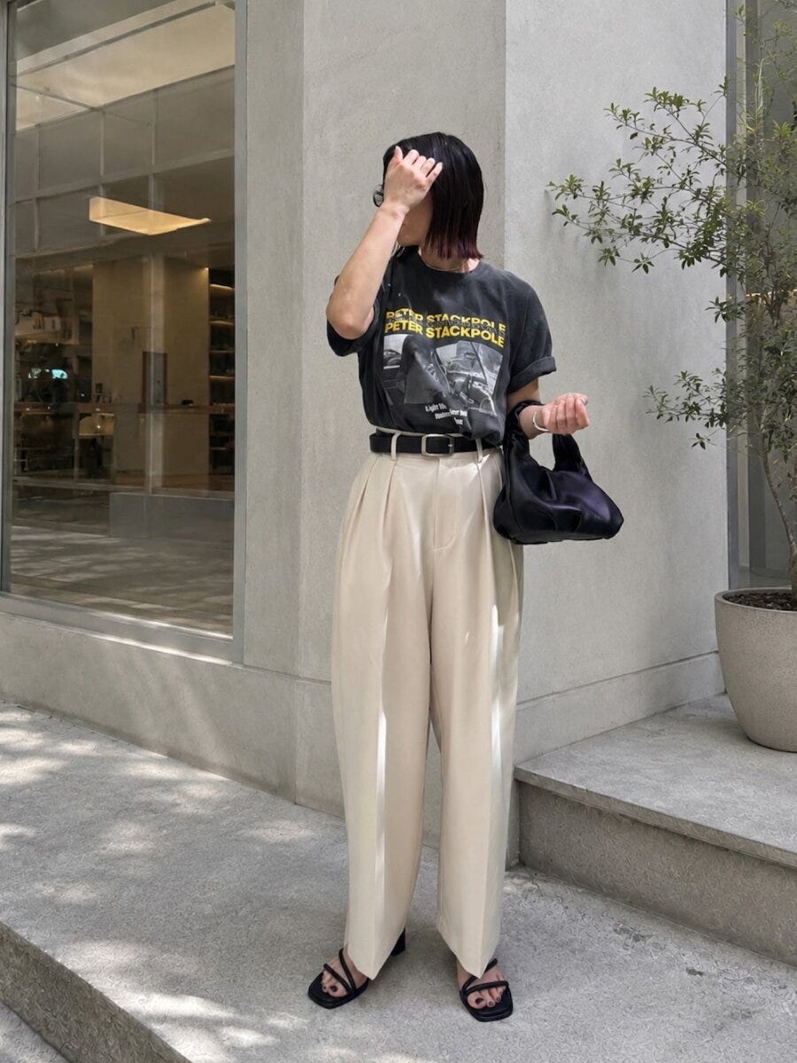 黒いフォトTシャツと白いワイドパンツを着た女性が黒いハンドバッグを持つ全身