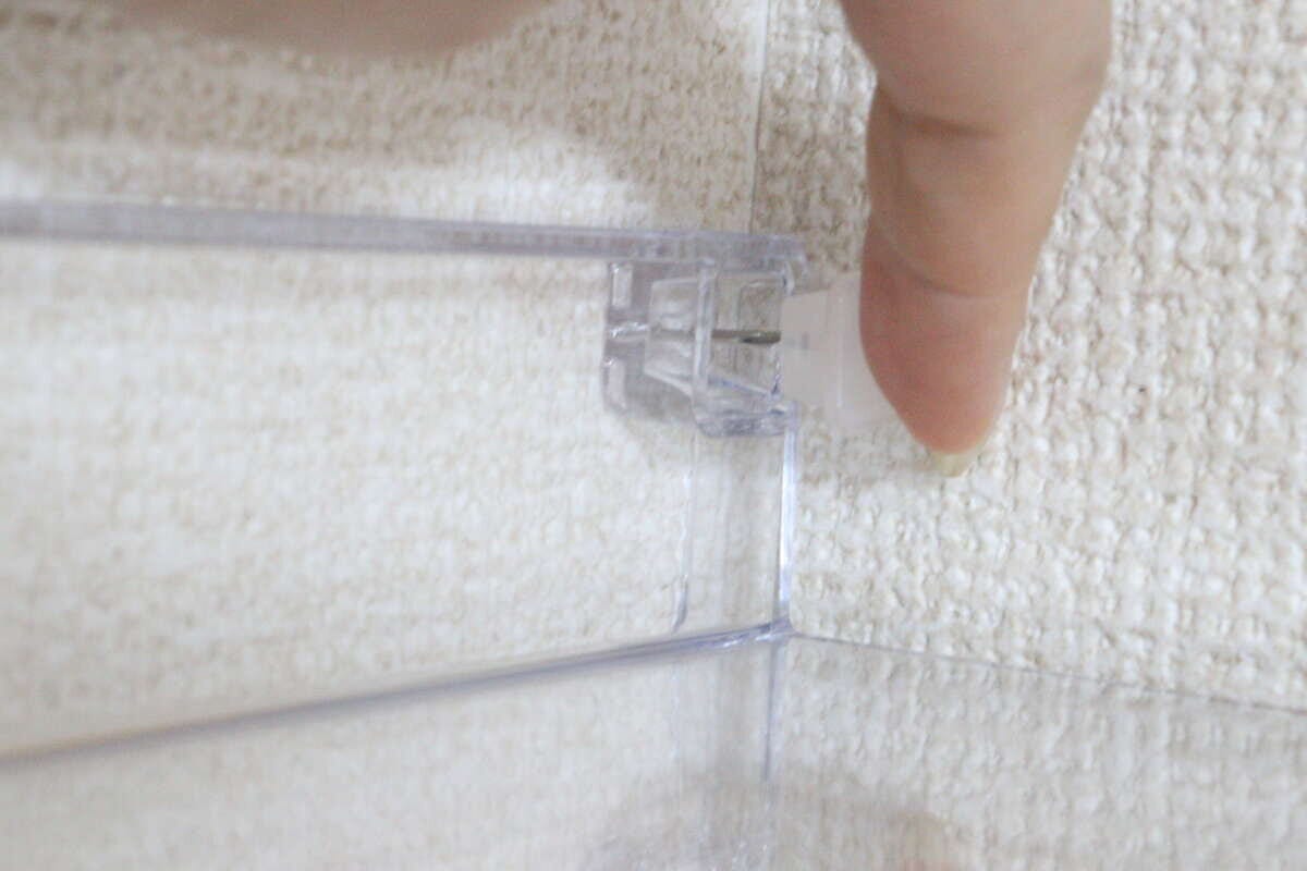 白い壁紙の壁にディスプレイトレーの穴の位置を合わせながら指でピンを押し込んでいる様子 白い壁紙の壁にディスプレイトレーの穴の位置を合わせながら指でピンを押し込んでいる様子