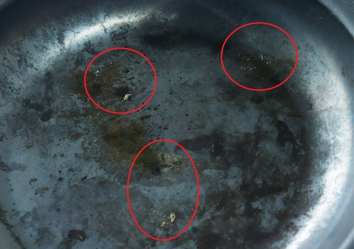 焦げ付きや油汚れが付着したフライパンの底を赤丸で囲んでいる 焦げ付きや油汚れが付着したフライパンの底を赤丸で囲んでいる