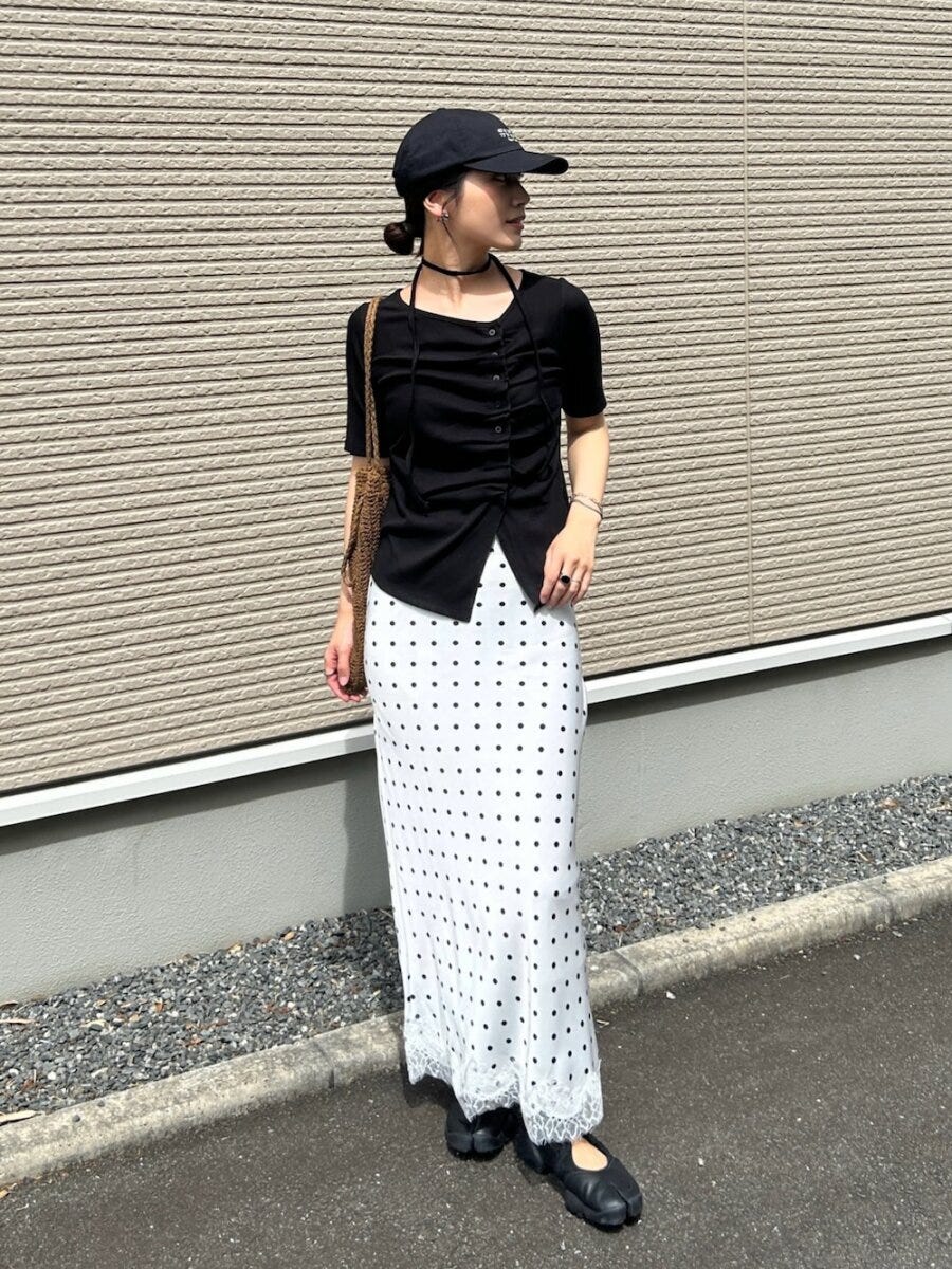 白ドット柄スカートに黒トップスとキャップを被った女性