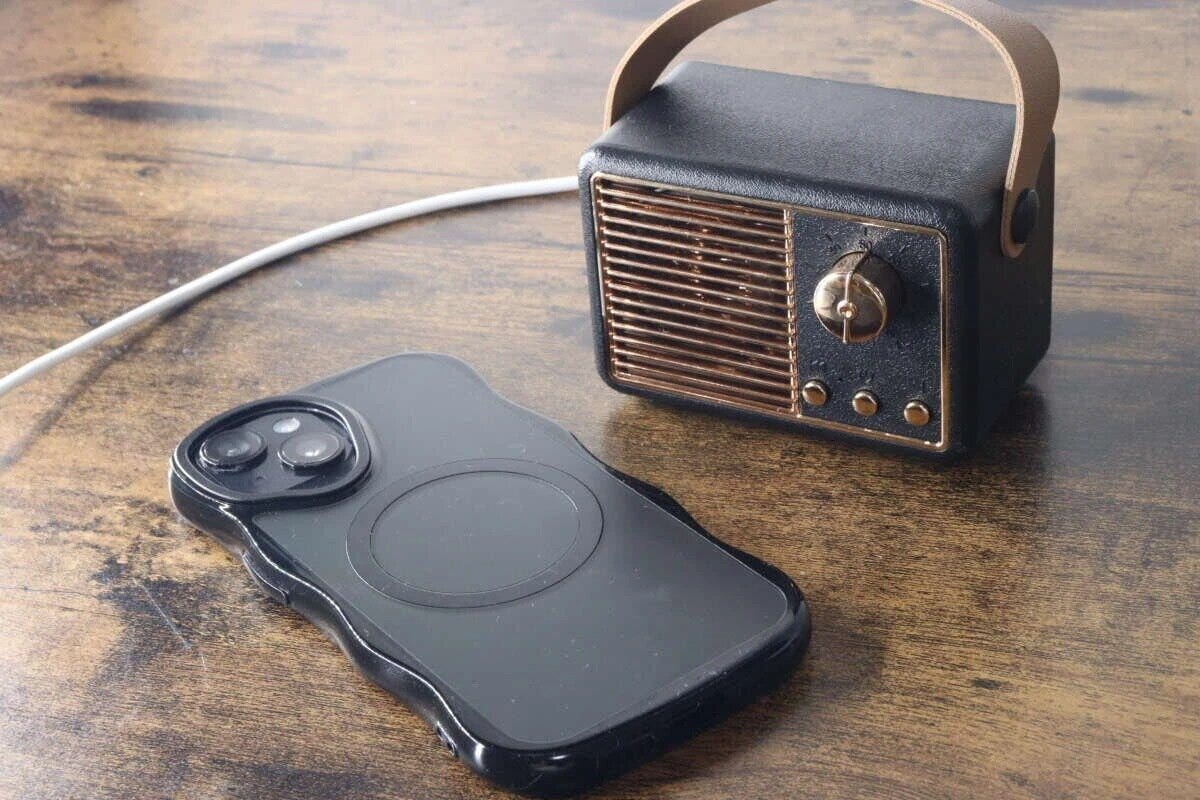 黒いラジオ型Bluetoothスピーカーの隣に、充電ケーブルが繋がれたスマートフォンが置かれている