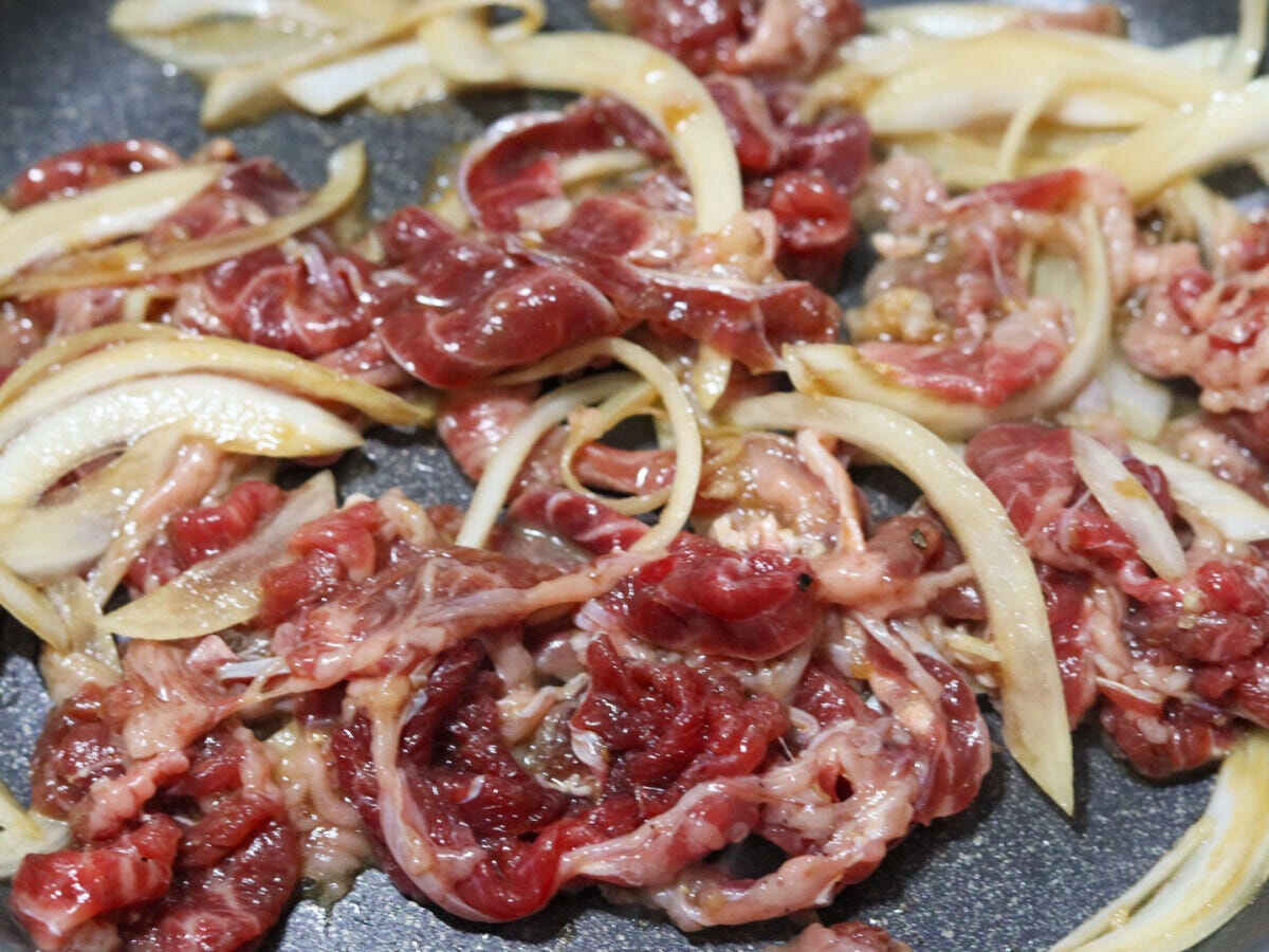 フライパンで漬け込んだ牛肉と玉ねぎをごま油で炒め始めた様子 フライパンで漬け込んだ牛肉と玉ねぎをごま油で炒め始めた様子
