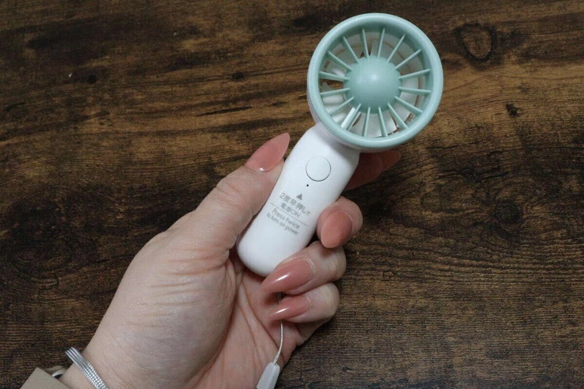 ピンクのネイルをした女性が淡い緑色のポータブルミニ扇風機を手に持つ