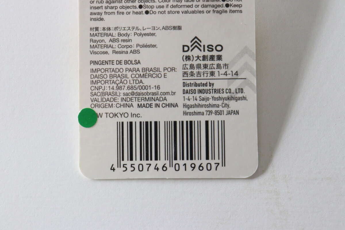 ダイソーのバッグチャームポーチの商品タグの裏面。JANコードや素材、販売元情報が記載されている。