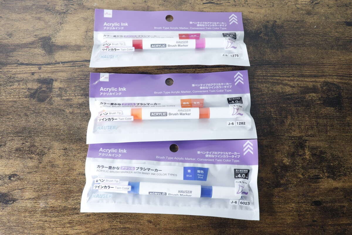 3つのアクリルブラシマーカーがパッケージに入った状態で木製のテーブルに置かれている