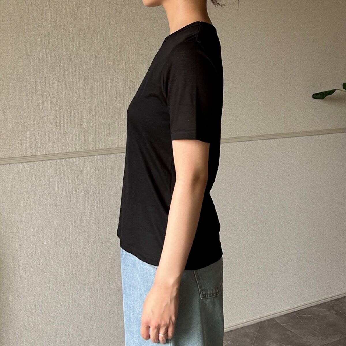 黒いシアーTシャツと薄いブルーのデニムパンツを着用した女性が横向きに立っている