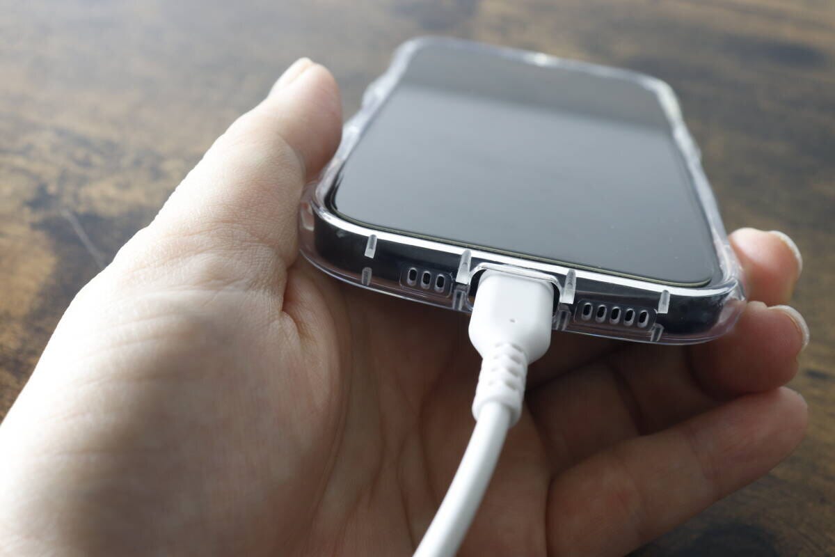 クリアケースを装着したiPhoneに充電ケーブルを挿し込んでいる手元