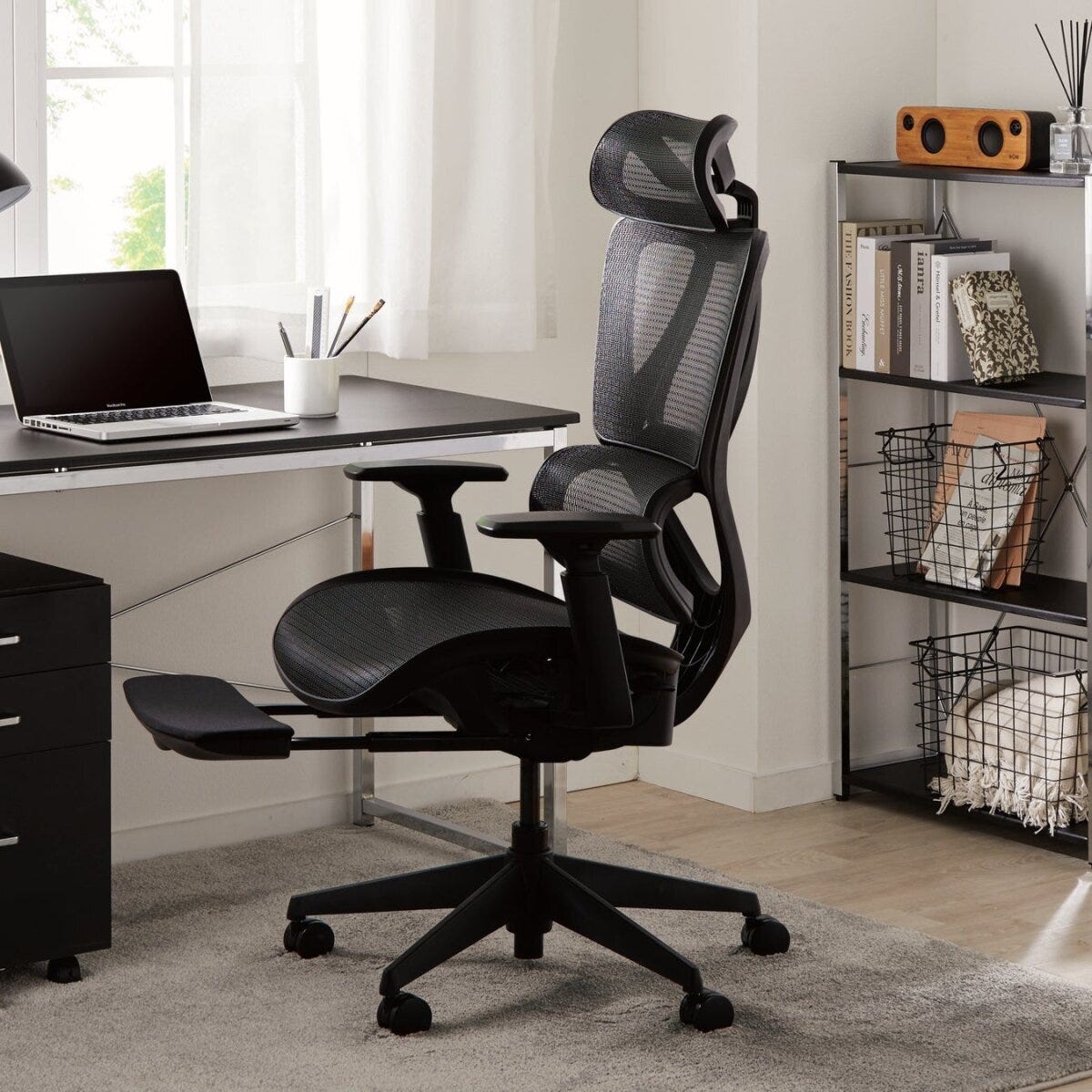 黒いメッシュ素材のオフィスチェアがデスクと棚のある部屋に置かれている