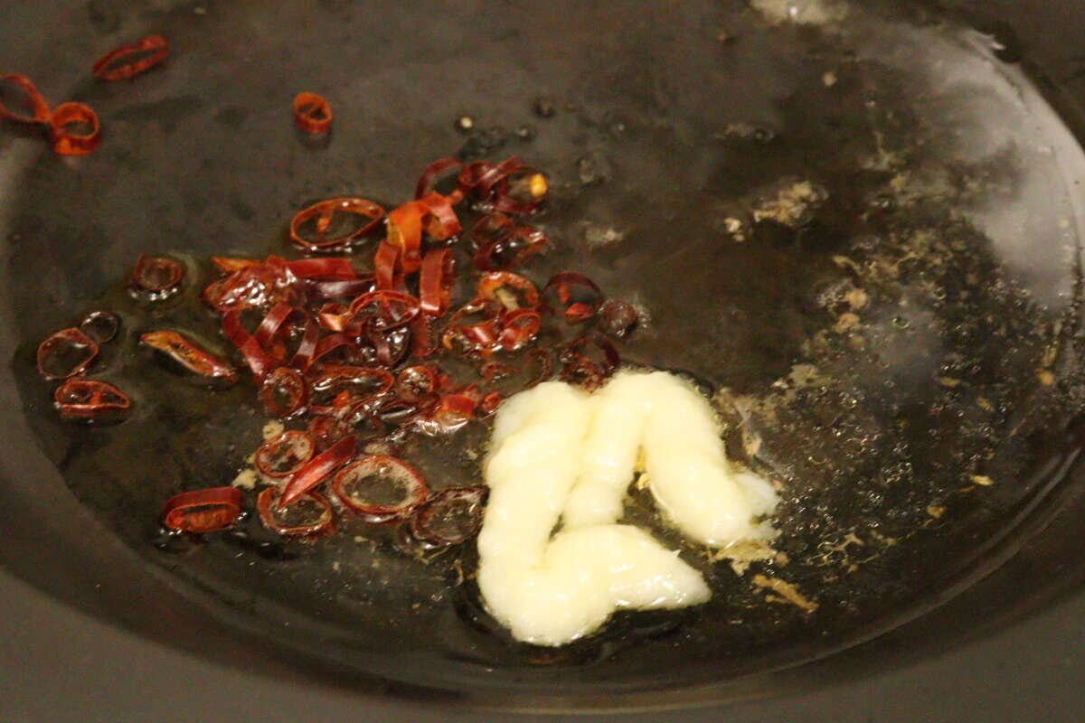 フライパンにいわし缶のオイル、にんにくチューブ、輪切り唐辛子が入っており、加熱されている様子 フライパンにいわし缶のオイル、にんにくチューブ、輪切り唐辛子が入っており、加熱されている様子