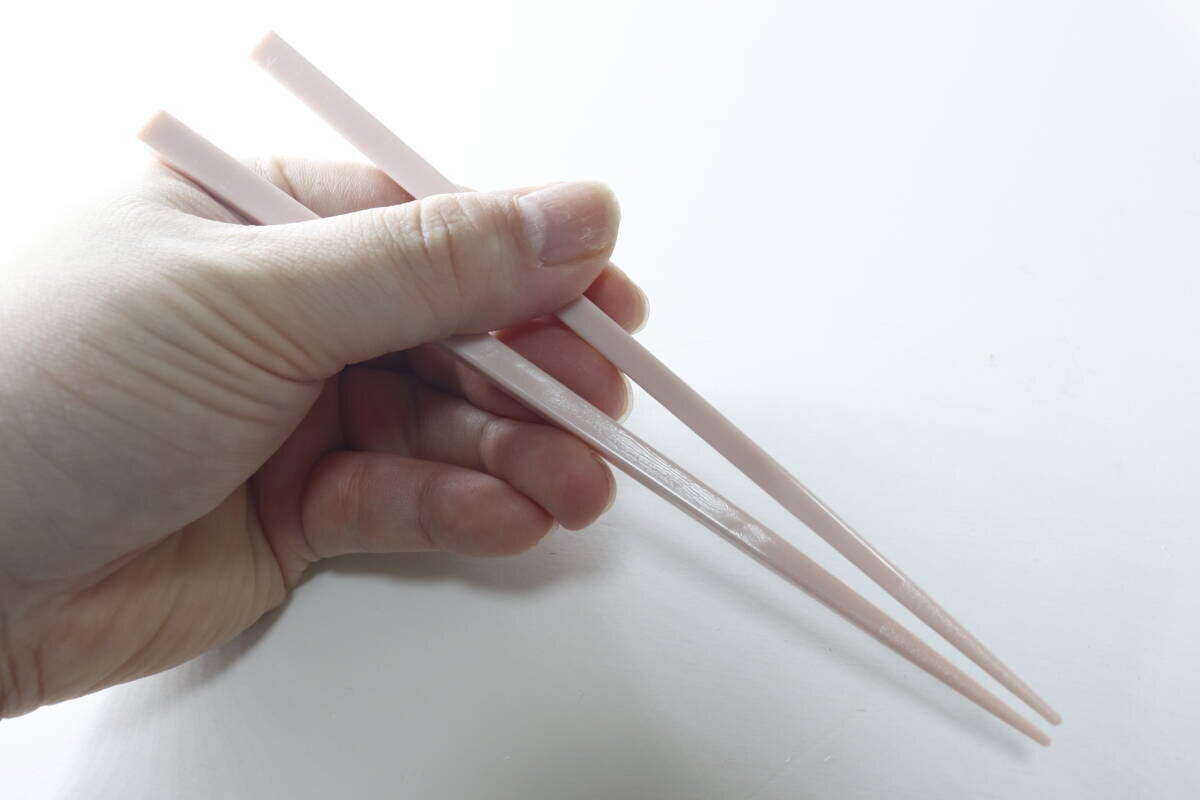 右手がピンク色の箸を持ち、先端の滑り止め部分が見える