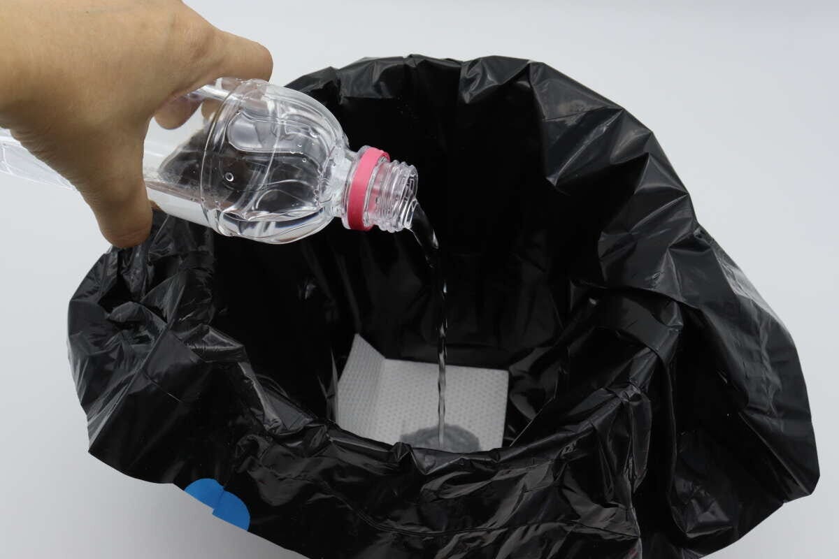 黒いビニール袋内の吸水シートにペットボトルから水を注ぐ