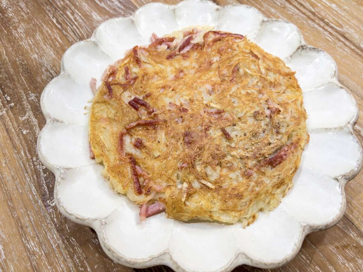 こんがりきつね色に焼きあがった新じゃがとベーコンのガレットを白い花型のお皿に盛り付けた完成写真