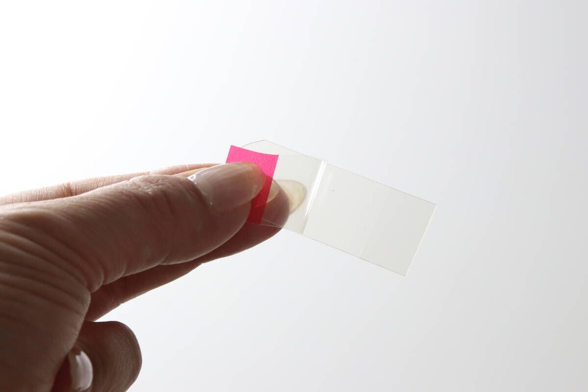 指で透明な伸びるテープの赤い保護フィルムを剥がしている様子