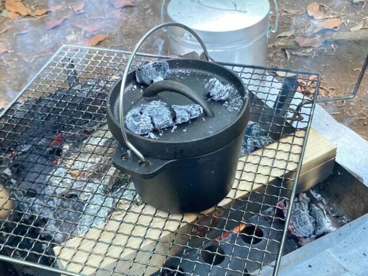 炭火の網の上に置かれた黒いダッチオーブンと炭