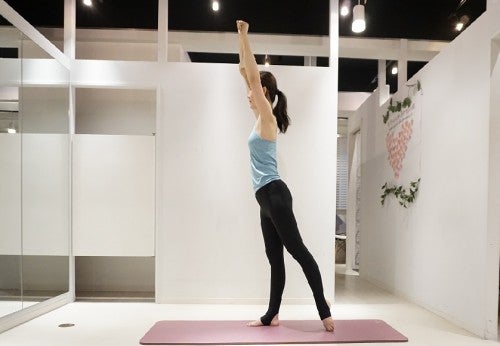 右足を軸にして立ち、左足を後ろに引きましょう。頭上で親指が内側に来るようにフェイスタオルをしっかり引っ張りながら持ちます。