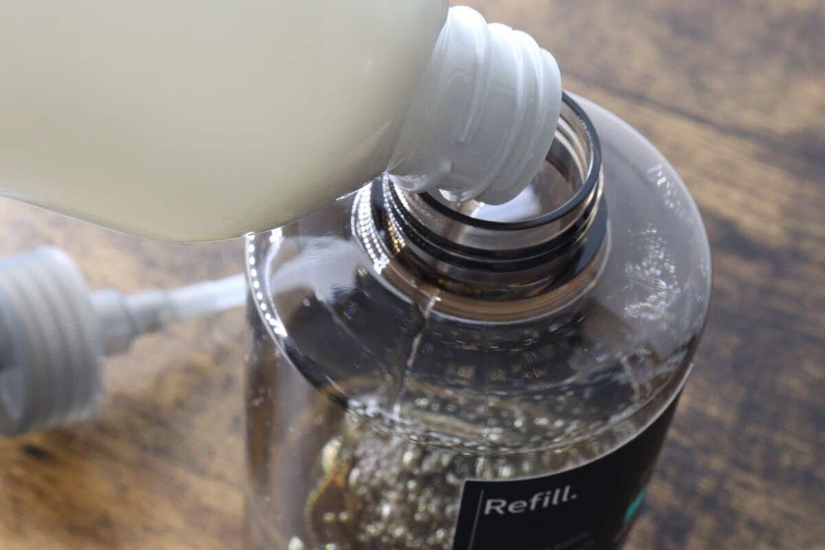白い洗剤ボトルからワンプッシュボトルに液体を注ぐ様子 白い洗剤ボトルからワンプッシュボトルに液体を注ぐ様子