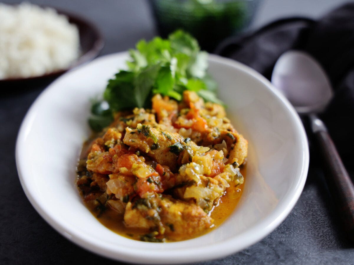 白い器に盛りつけた鶏むね肉とパクチーのカレーにパクチーをトッピングした完成写真