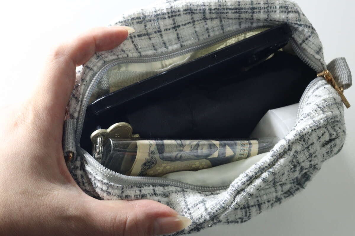女性の手が、チェック柄のポーチに黒い折りたたみ傘を収納している様子