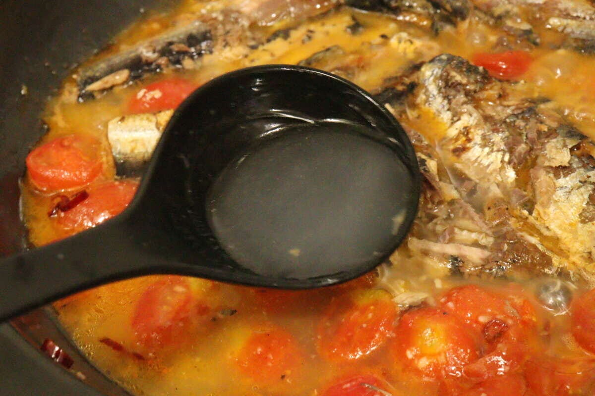 フライパンで煮込まれている具材に、黒いお玉でパスタのゆで汁が加えられている瞬間 フライパンで煮込まれている具材に、黒いお玉でパスタのゆで汁が加えられている瞬間