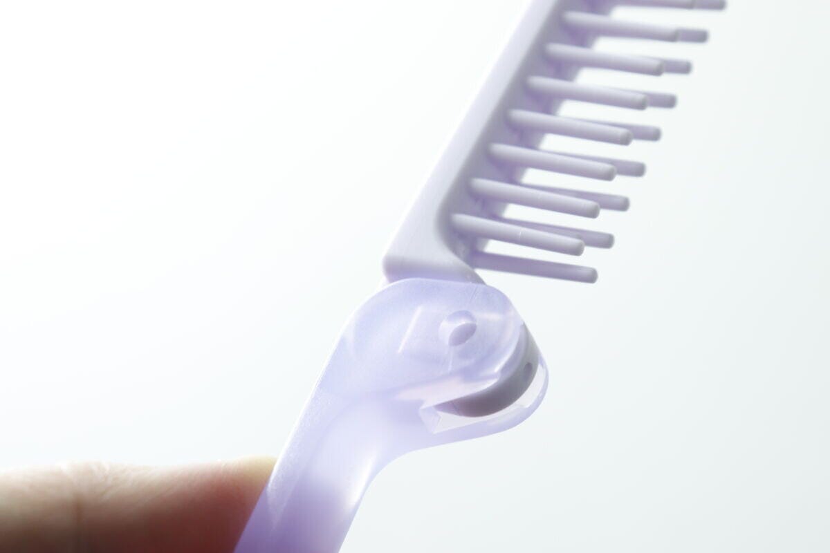指で持たれたヘアブラシの折りたたみ部分の接合部