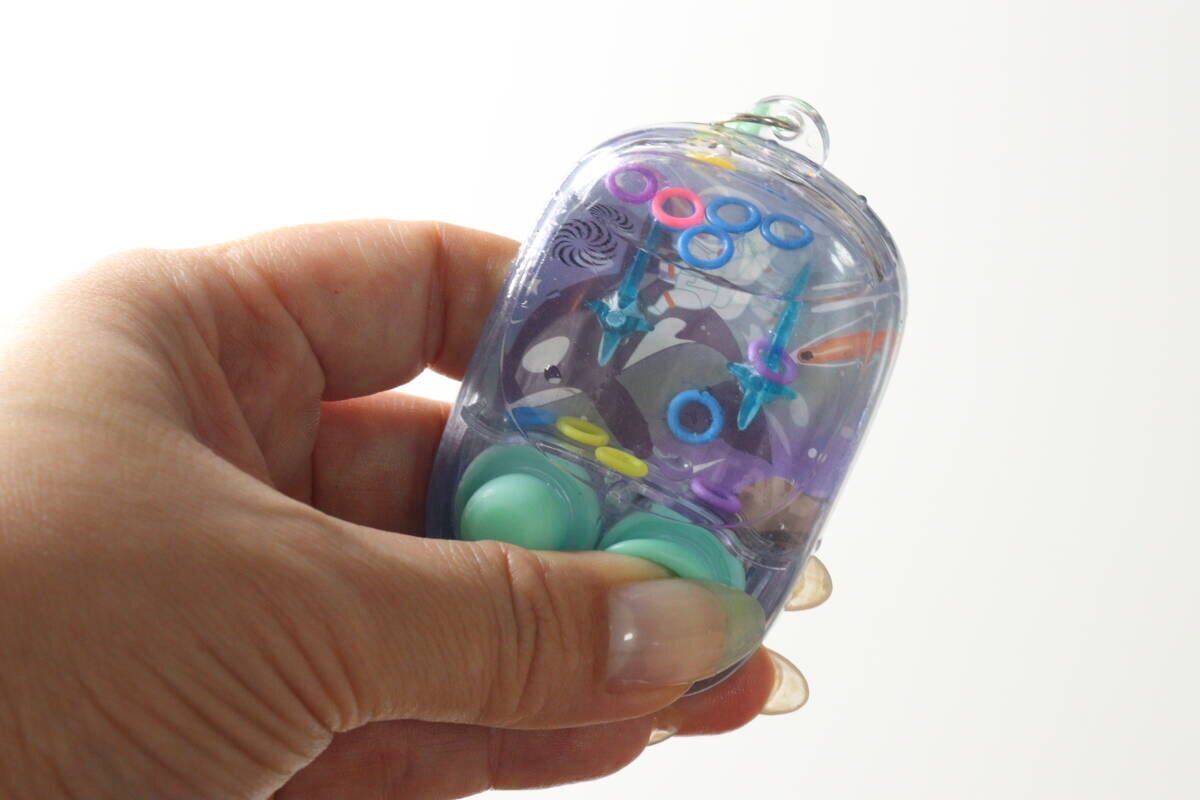 水が満たされ、輪っかが浮いているミニウォーターゲーム機を手に持っている 水が満たされ、輪っかが浮いているミニウォーターゲーム機を手に持っている