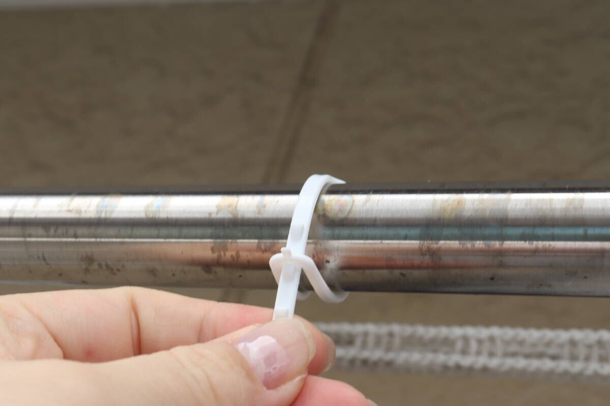 物干し竿に白いピンチの紐を結びつける手元 物干し竿に白いピンチの紐を結びつける手元